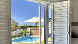 Habitació amb porta de vidre corredissa que dona a una zona de piscina, una cuina petita i una sortida visible.