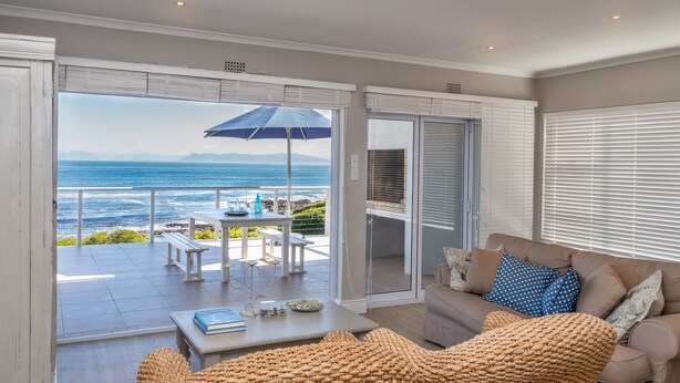 A living room with a view of the ocean, a sofa, a coffee table, and a dining area with outdoor seating.