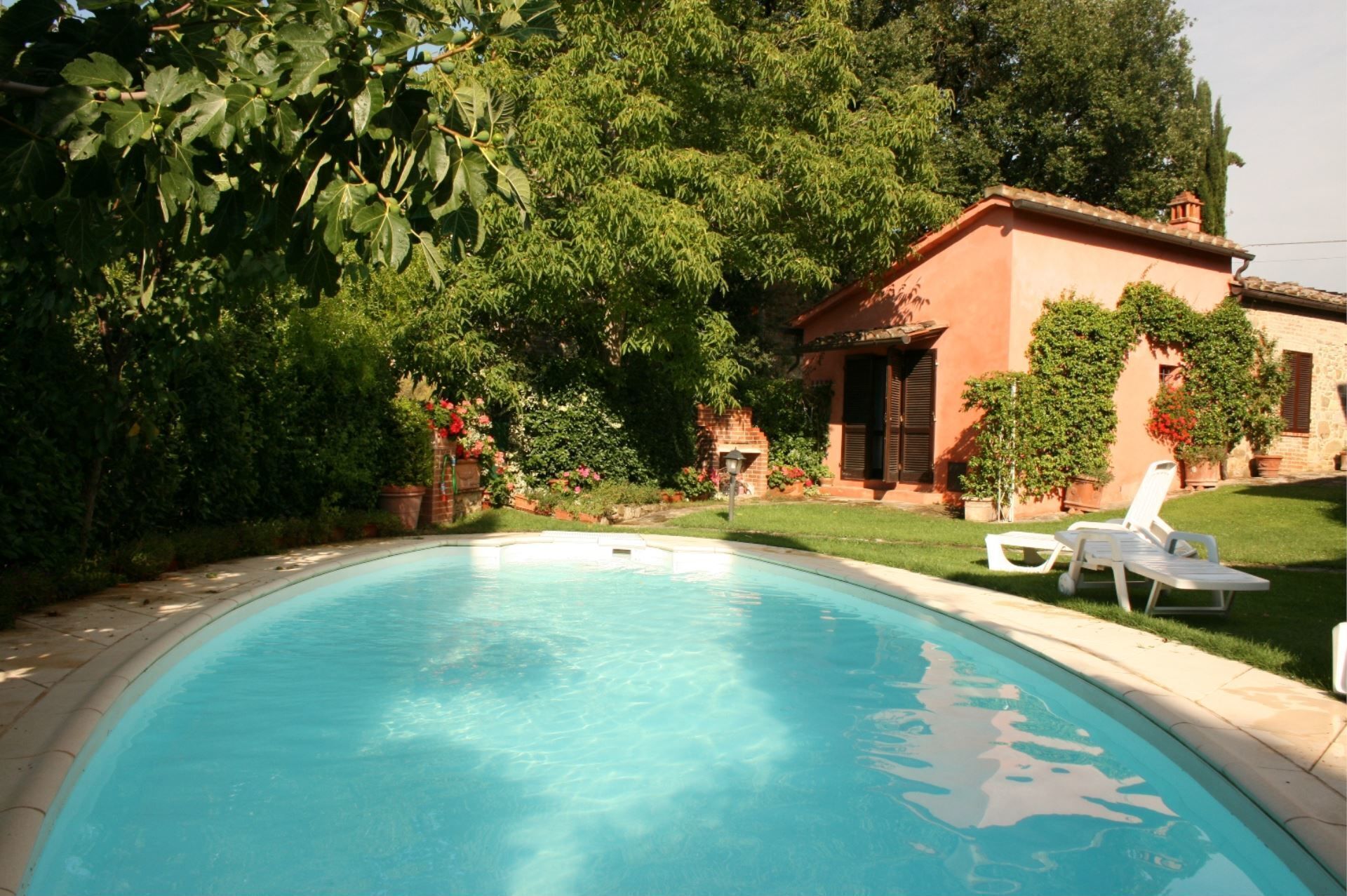 A swimming pool with a clear blue water, surrounded by lush greenery and a building with a red facade.