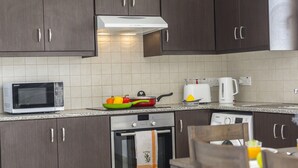 A kitchen with dark wooden cabinets, a microwave, an oven, a kettle, and a fruit bowl. - Protaras Palm Suite 207 (Protaras)