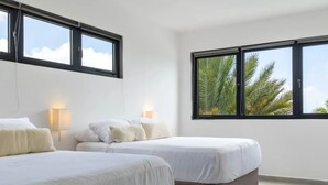 Habitación de hotel con dos camas, ventanas amplias y vistas a palmeras.