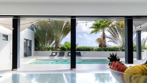 Un área de piscina moderna con agua cristalina, sillas de descanso y plantas tropicales.