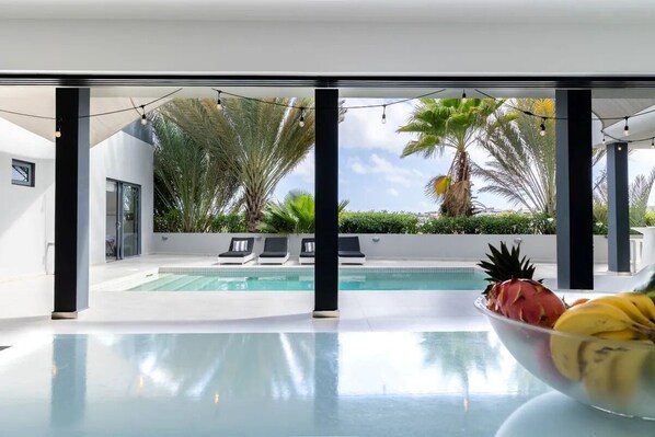 A modern pool area with clear blue water, lounge chairs, and tropical plants.