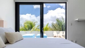 Un dormitorio moderno con una cama grande, una puerta corrediza de vidrio que da a un balcón con mobiliario exterior.