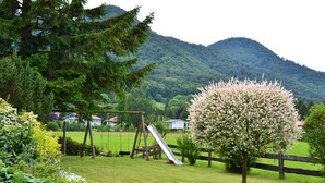 A playground with a slide and swings, surrounded by lush greenery and flowering plants. - No.4 Apartment 50 sqm with one separate bedroom, kitchen-living room, east-facing balcony (Aschau im Chiemgau)