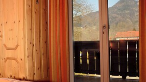 A bedroom with a large bed, wooden wardrobe, and a sliding glass door leading to a balcony with a mountain view. - No.4 Apartment 50 sqm with one separate bedroom, kitchen-living room, east-facing balcony (Aschau im Chiemgau)