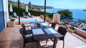 Un espacio de estar al aire libre cubierto con mesa, sillas y sombrillas, con vistas a un paisaje costero.