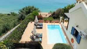 Una piscina con sillones de descanso y vista al mar.