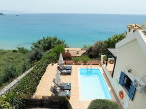 A pool with lounge chairs and a view of the sea.