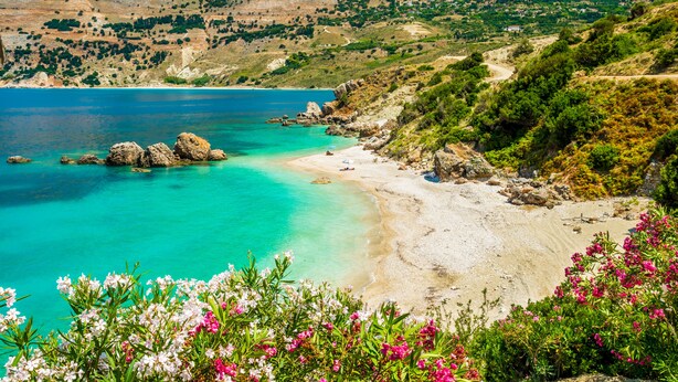 Un paisaje costero con un mar turquesa transparente, una playa arenosa y afloramientos rocosos.