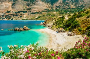 A coastal landscape with a clear turquoise sea, sandy beach, and rocky outcrops.