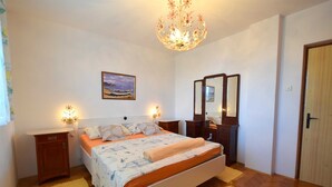 Un dormitorio con cama, mesitas de noche, cómoda, espejo, candelabro y un cuadro en la pared.