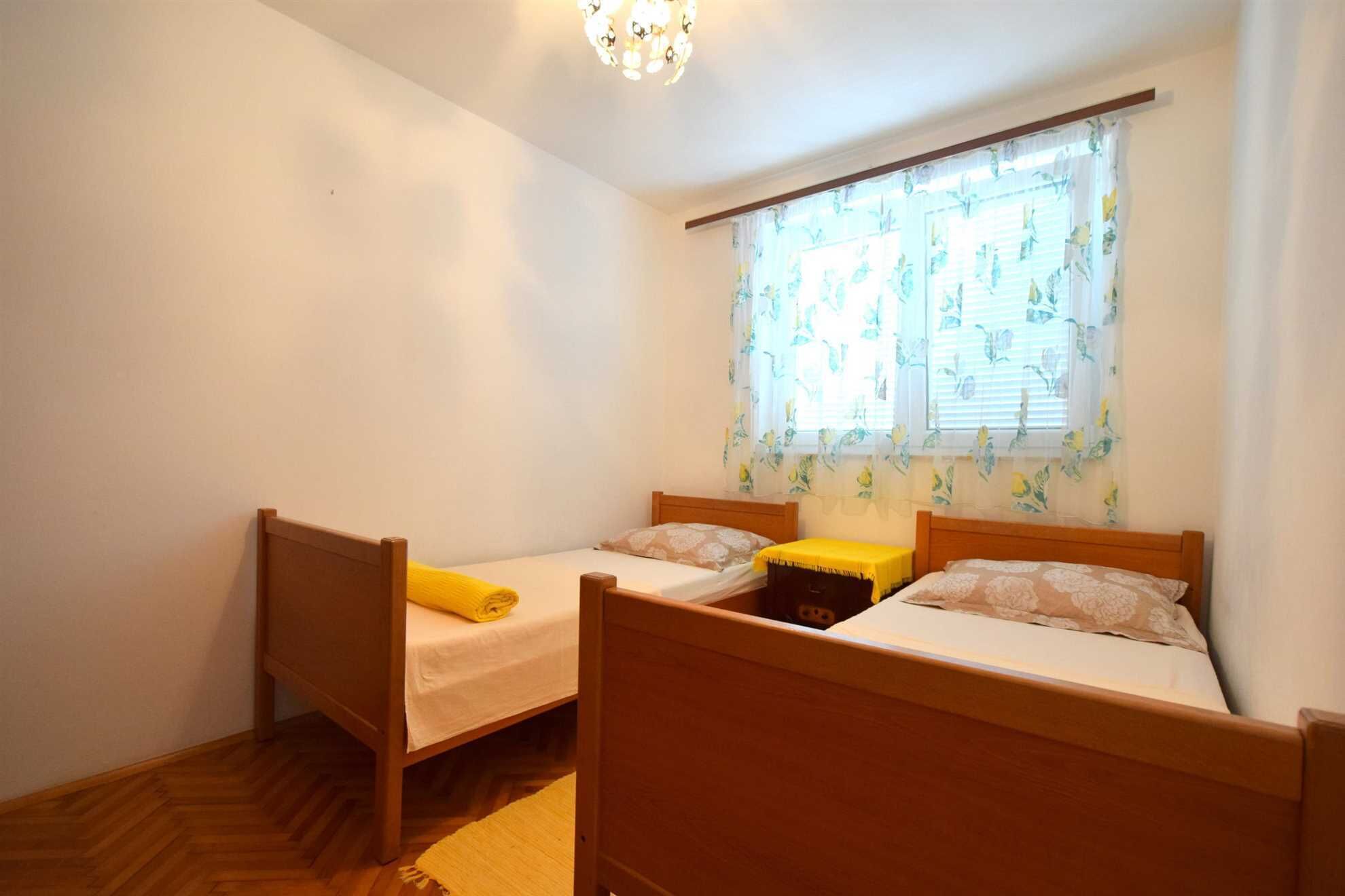 Una habitación con dos camas de madera, un ventanal con cortinas florales y suelo de madera.