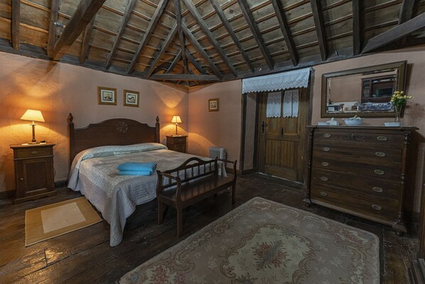 Un dormitorio con techo de madera, una cama con manta azul, un aparador de madera y un espejo encima.