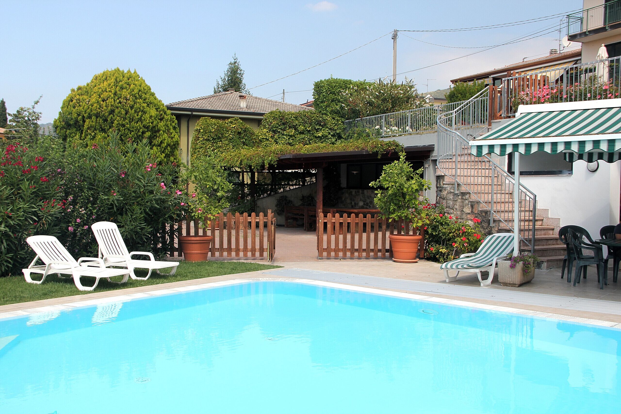 Una piscina con sillas de descanso, una valla de madera y plantas en macetas.