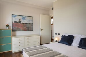 A bedroom with a bed, a dresser, a painting, and a door leading to another room. - Apartment Montegolo Four With Pool And Lake View (Costermano)