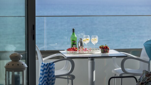 Un balcon avec une table dressée pour deux personnes, agrémentée d’une bouteille, de verres et d’un panier de fruits.