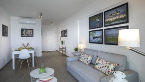 Un salon moderne avec un canapé gris, une table à manger avec des chaises et une petite table ronde surmontée d’une lampe.