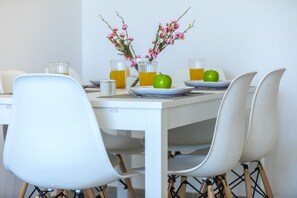 A dining table with chairs, a vase with flowers, a green apple, and glasses of orange juice.