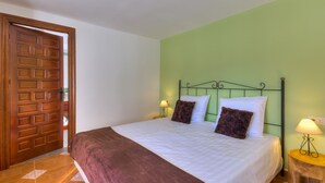 A bedroom with a wooden door, a green wall, a bed with white and brown bedding, two bedside lamps, and a small wooden nightstand. - Villa Damara, luxury apartment Oliva, the place to relax! (Albox)