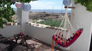 A hammock chair hanging from a white wall, a wooden table with a pink candle, and a view of a mountainous landscape. - Villa Damara, luxury apartment Oliva, the place to relax! (Albox)