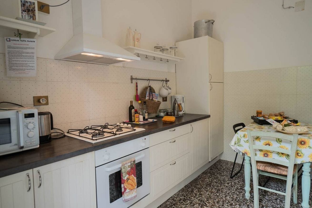 Una cucina con mobili bianchi, piano cottura a gas, forno a microonde e tavolo con tovaglia a fiori di girasole.