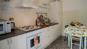 Une cuisine avec des meubles blancs, une cuisinière à gaz, un four à micro-ondes et une table recouverte d’une nappe à motifs de tournesols.