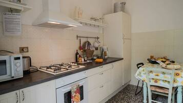 Una cucina con mobili bianchi, piano cottura a gas, forno a microonde e tavolo con tovaglia a fiori di girasole.