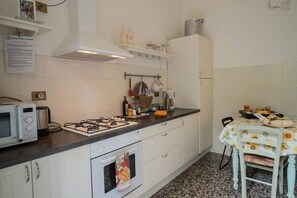 Una cocina con armarios blancos, estufa a gas, microondas y una mesa con mantel de girasoles.