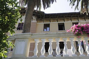 A building with a balcony, a palm tree, and pink flowers.