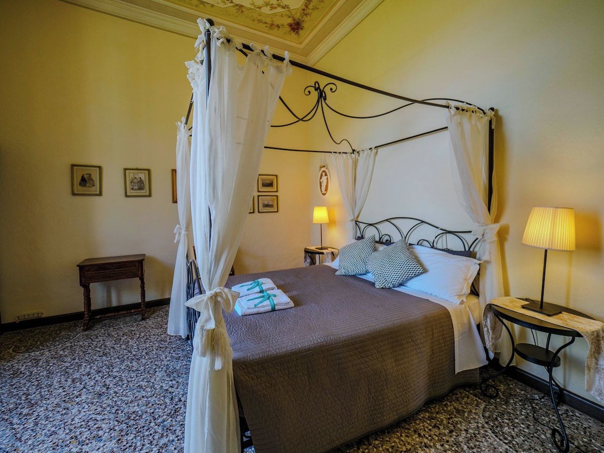 A four-poster bed with a canopy, a bedside table with a lamp, and a small nightstand.
