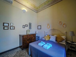 A bedroom with a bed, dresser, bedside table, lamp, and wall decorations. - Villa Montale Historical Apartment I Limoni (Monterosso al Mare)
