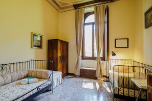Une pièce avec deux lits, un radiateur, une fenêtre avec des rideaux, une armoire en bois et un tableau encadré au mur.