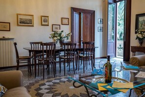Un comedor con una mesa redonda y sillas, un florero con flores y una botella de vino sobre una mesa de vidrio.