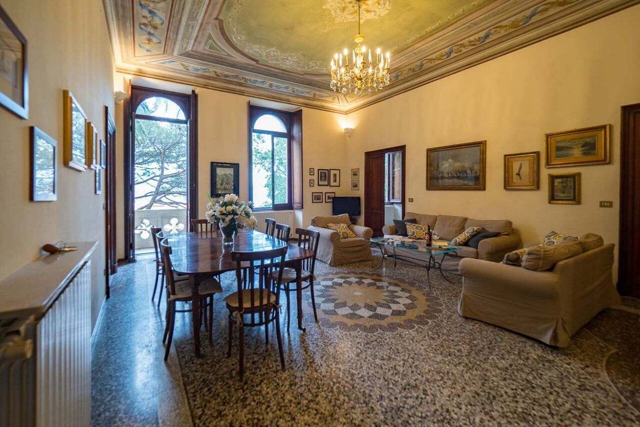 Una stanza con un tavolo da pranzo, sedie, un divano e un lampadario.