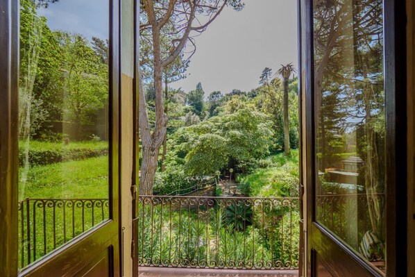 A view through a glass door with a metal railing, leading to a lush garden with various trees and shrubs. - Villa Montale Apartment I Limoni (Monterosso al Mare)