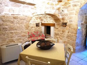 Um quarto com paredes de pedra, uma mesa, cadeiras, um sofá floral e uma lareira.