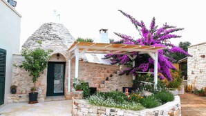 Ett stenhus med en stenkupol, en täckt uteplats med en pergola och färgstarka bougainvilleablommor.