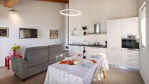 Eine moderne Küche mit weißen Schränken, einem Esstisch für vier Personen und einem grauen Sofa im Wohnbereich.