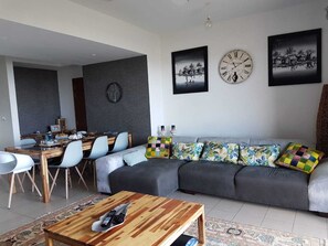 Ein modernes Wohnzimmer mit einer grauen Couch, einem Holztisch und einem Essbereich mit Holztisch und weißen Stühlen.