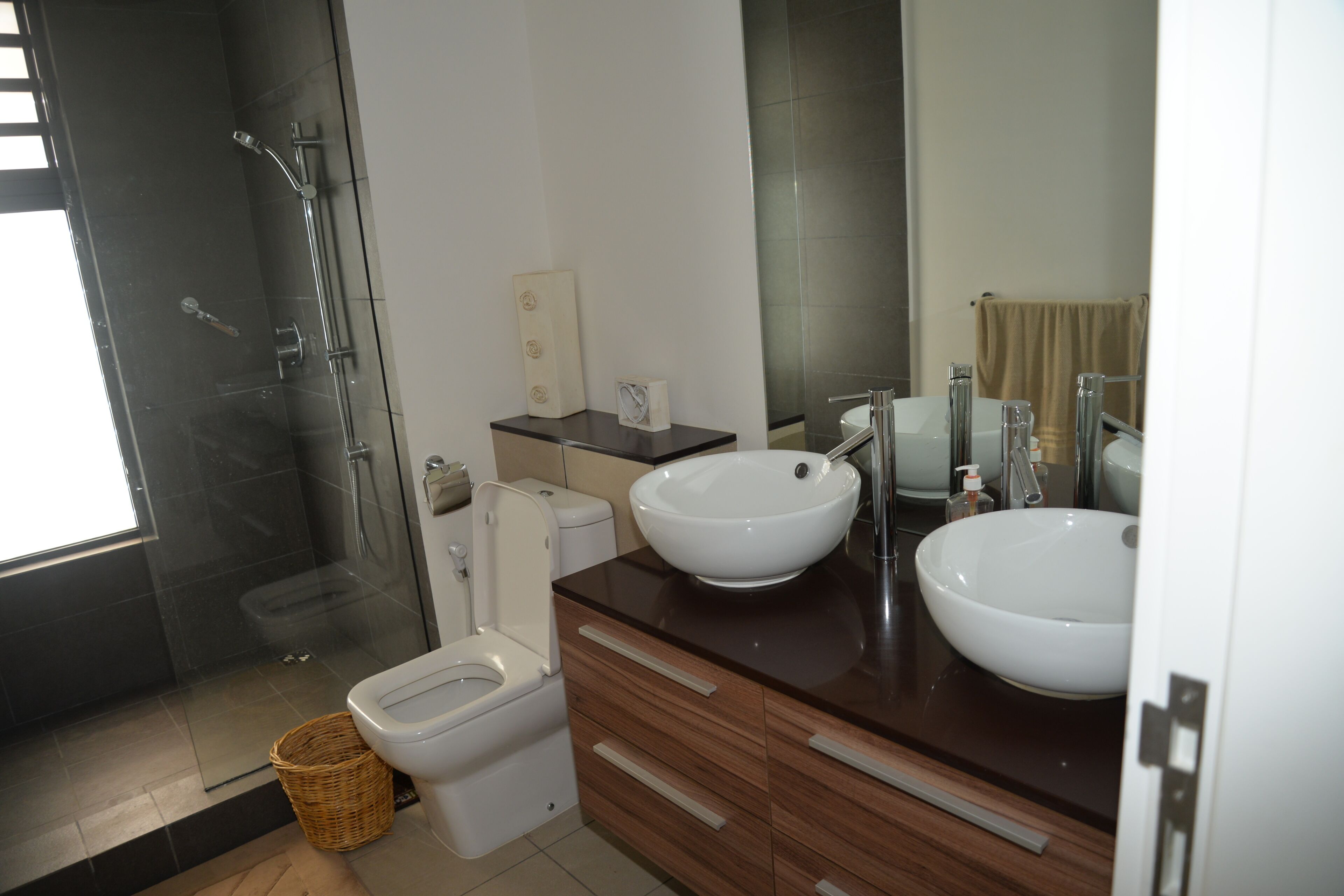 Une salle de bain moderne avec une douche à parois de verre, des toilettes et deux vasques sur un meuble-lavabo en bois.