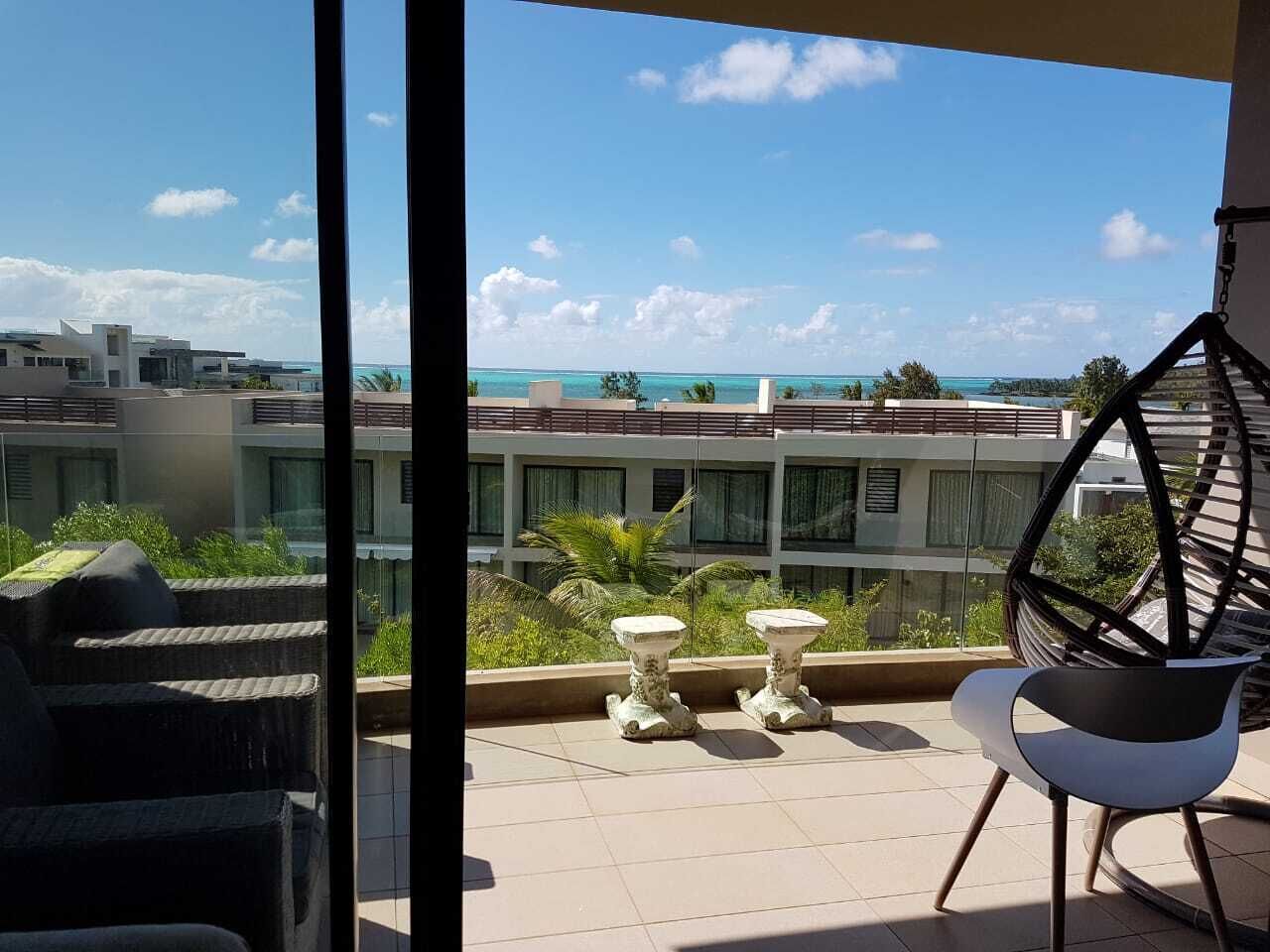 Uma varanda com vista para o oceano, uma cadeira suspensa e duas pequenas mesas.