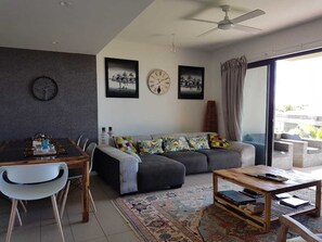 Ein modernes Wohnzimmer mit Essbereich, einer Couch, einem Couchtisch und einem großen Fenster mit Vorhängen.