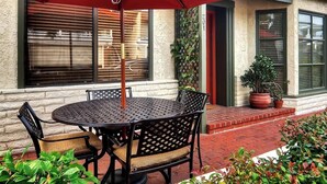 Un patio con un tavolo rotondo e sedie, un ombrellone rosso e piante in vaso.