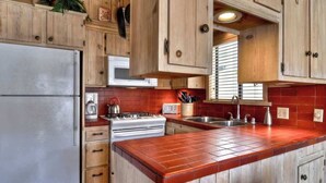Una cucina con mobili in legno, un frigorifero in acciaio inossidabile, un fornello e un piano di lavoro rivestito di piastrelle rosse.