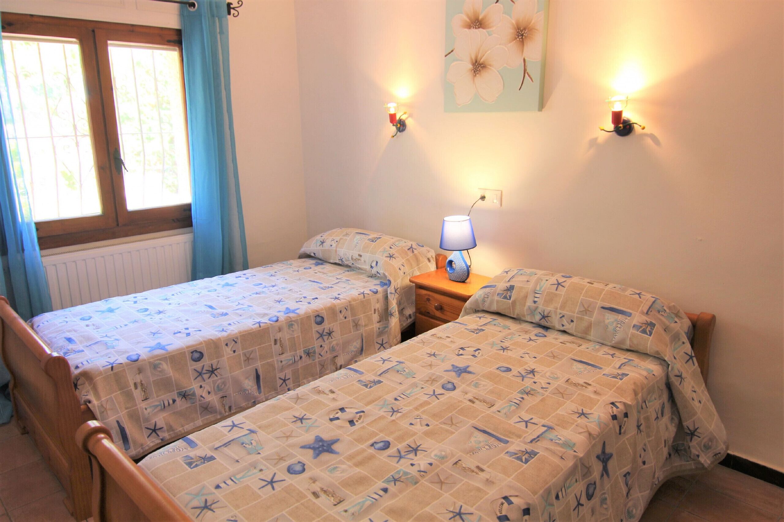 Een slaapkamer met twee bedden, een nachtkastje, een lamp, een raam met gordijnen en wandlampen.