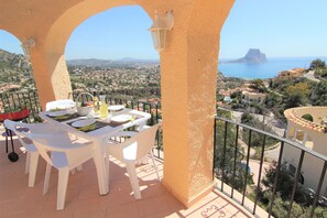 Un balcon avec une table dressée pour deux personnes, offrant une vue sur une ville côtière et la mer.