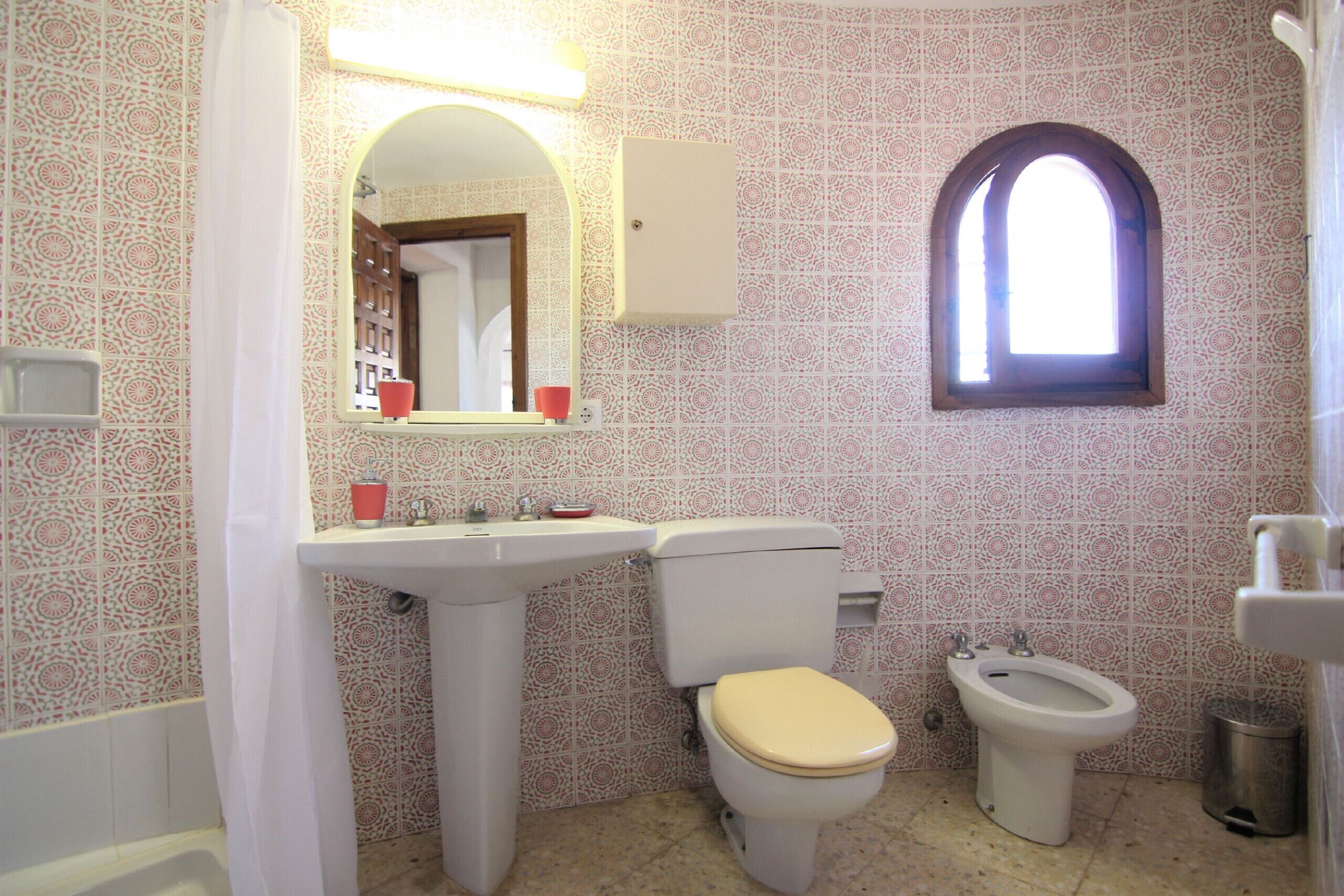 A bathroom with a toilet, bidet, sink, and a window.