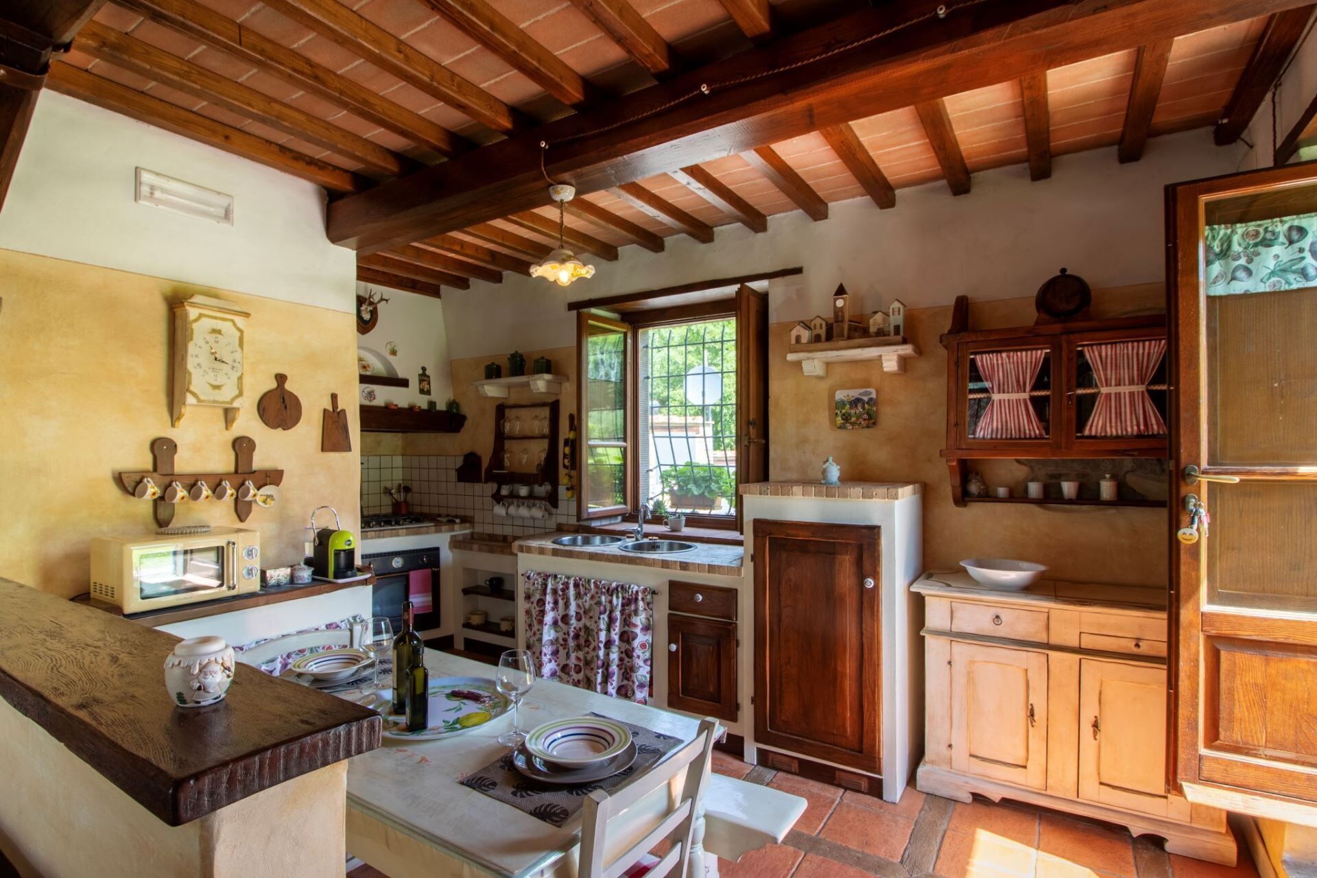 Una cocina rústica con vigas de madera, estufa, lavabo y comedor con una mesa dispuesta para dos.
