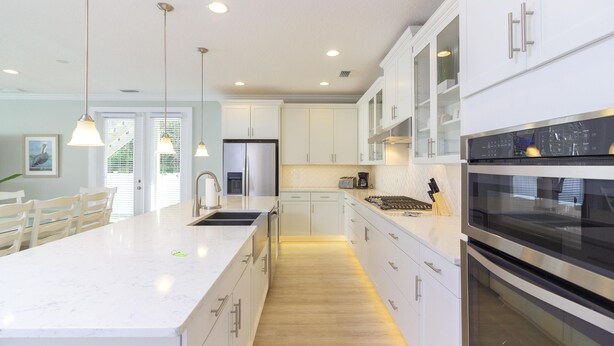 Una cocina moderna con armarios blancos, una isla grande, electrodomésticos de acero inoxidable e iluminación colgante.